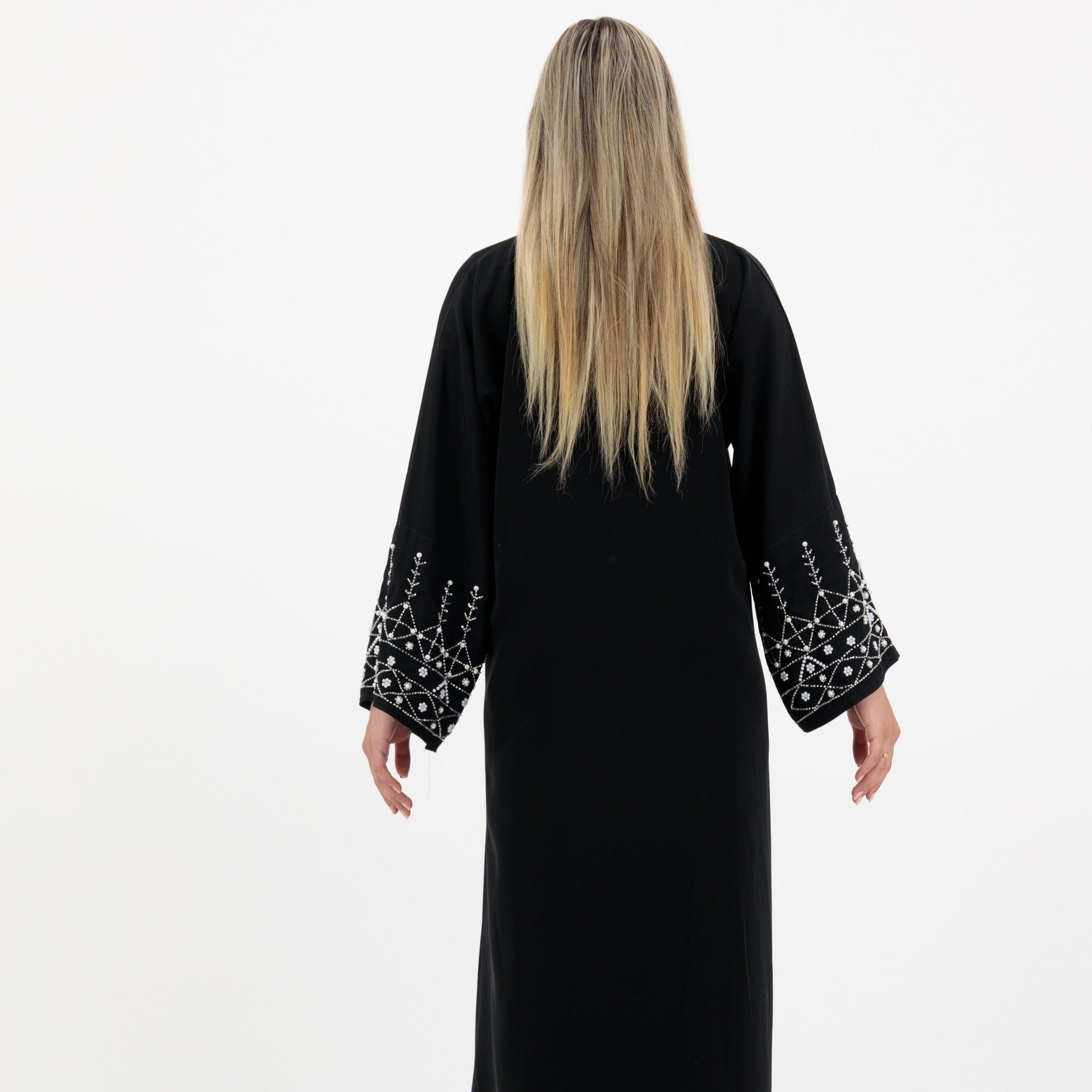 Black abaya in sizes 50-60 with hand-sewn silver and white pearl-like beadwork on the arms. Made from Zoom fabric, it features popper buttons and includes a matching black hijab. Handwash to preserve beadwork.