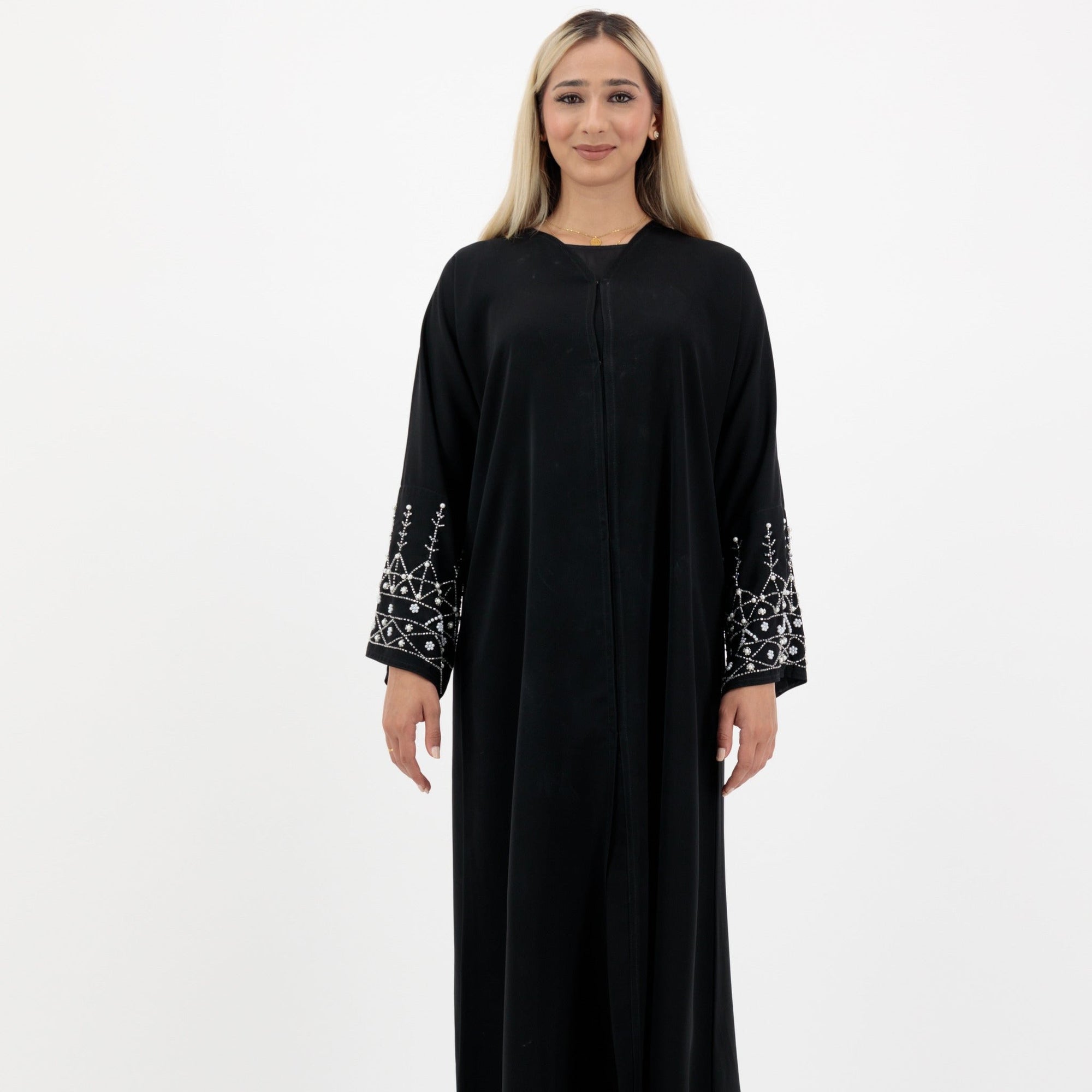 Black abaya in sizes 50-60 with hand-sewn silver and white pearl-like beadwork on the arms. Made from Zoom fabric, it features popper buttons and includes a matching black hijab. Handwash to preserve beadwork.