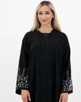 Black abaya in sizes 50-60 with hand-sewn silver and white pearl-like beadwork on the arms. Made from Zoom fabric, it features popper buttons and includes a matching black hijab. Handwash to preserve beadwork.