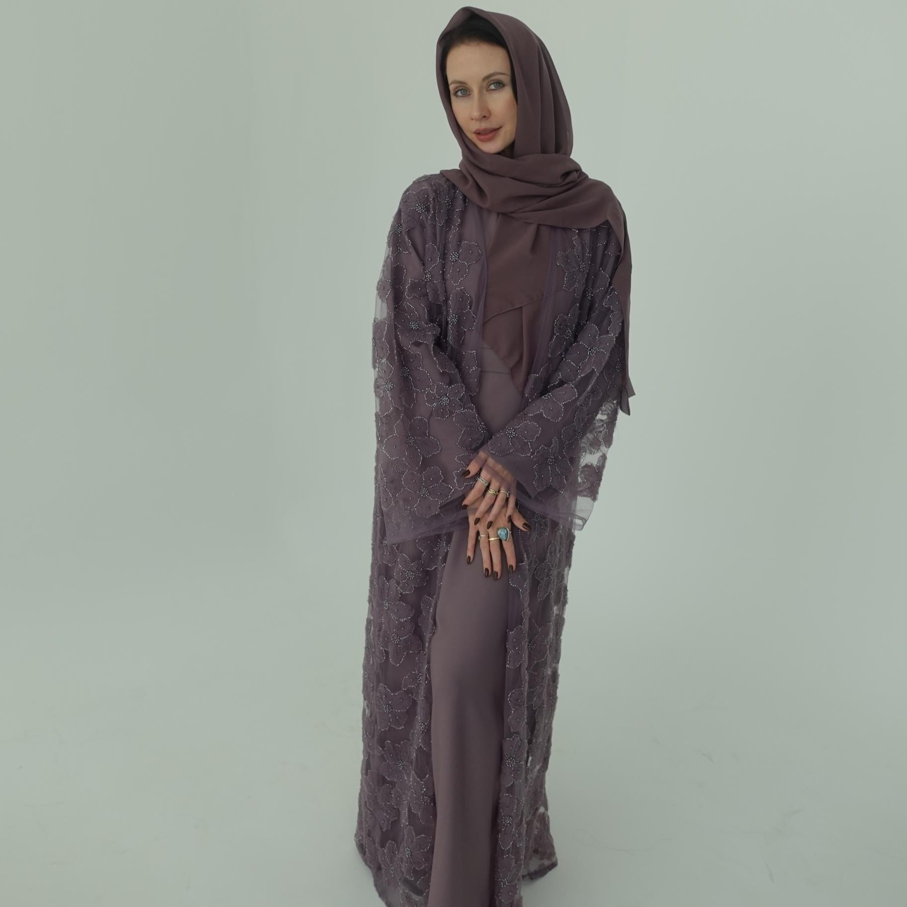 Woman wearing a long, dark purple dress with a matching hijab on a light gray background