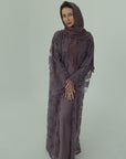 Woman wearing a long, dark purple dress with a matching hijab on a light gray background