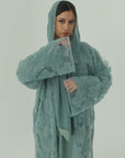 Person wearing a textured green robe against a plain background
