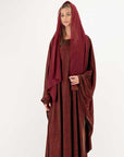 Woman wearing a long burgundy dress with a hood on a white background
