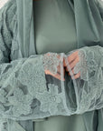 Woman wearing a light green abaya with floral embroidery on sleeves against a neutral background