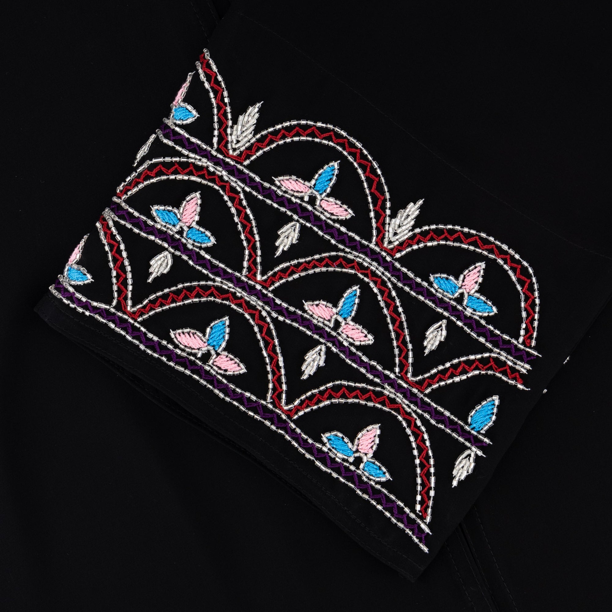 Black Liana Abaya with hand-sewn silver beads in a leaf and embroidery design pattern on the arms. Light pink, blue, and purple threads add color to the embroidery. Comes with a matching black hijab and popper buttons for closure.