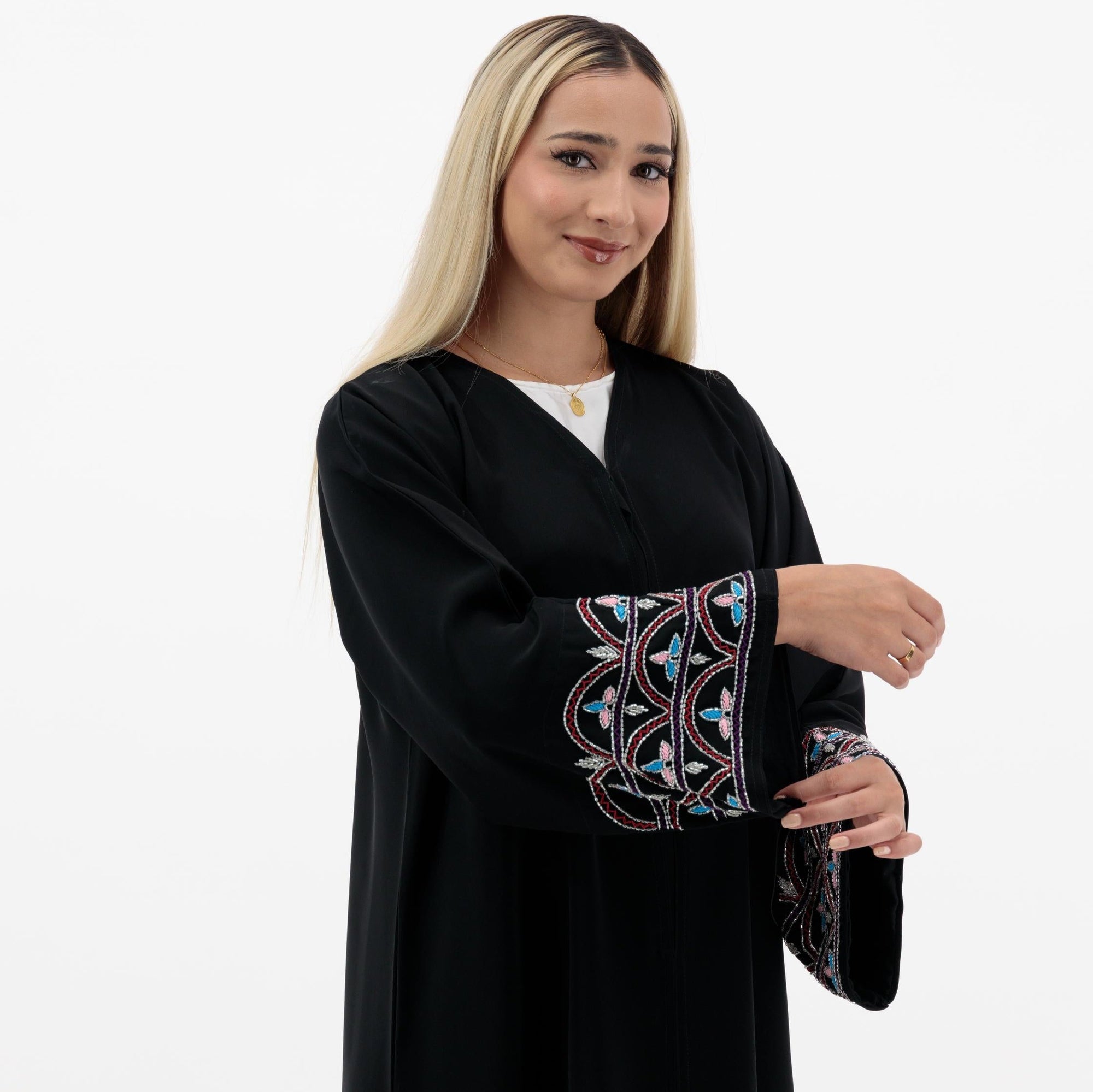 Black Liana Abaya with hand-sewn silver beads in a leaf and embroidery design pattern on the arms. Light pink, blue, and purple threads add color to the embroidery. Comes with a matching black hijab and popper buttons for closure.
