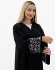 Black Liana Abaya with hand-sewn silver beads in a leaf and embroidery design pattern on the arms. Light pink, blue, and purple threads add color to the embroidery. Comes with a matching black hijab and popper buttons for closure.