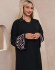 Black Liana Abaya with hand-sewn silver beads in a leaf and embroidery design pattern on the arms. Light pink, blue, and purple threads add color to the embroidery. Comes with a matching black hijab and popper buttons for closure.