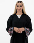 Black Liana Abaya with hand-sewn silver beads in a leaf and embroidery design pattern on the arms. Light pink, blue, and purple threads add color to the embroidery. Comes with a matching black hijab and popper buttons for closure.