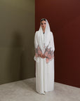 White abaya with silver beadwork and pink and brown embroidery on the sleeves. Made from crepe material with popper buttons, available in sizes 50-60, and includes a matching hijab.
