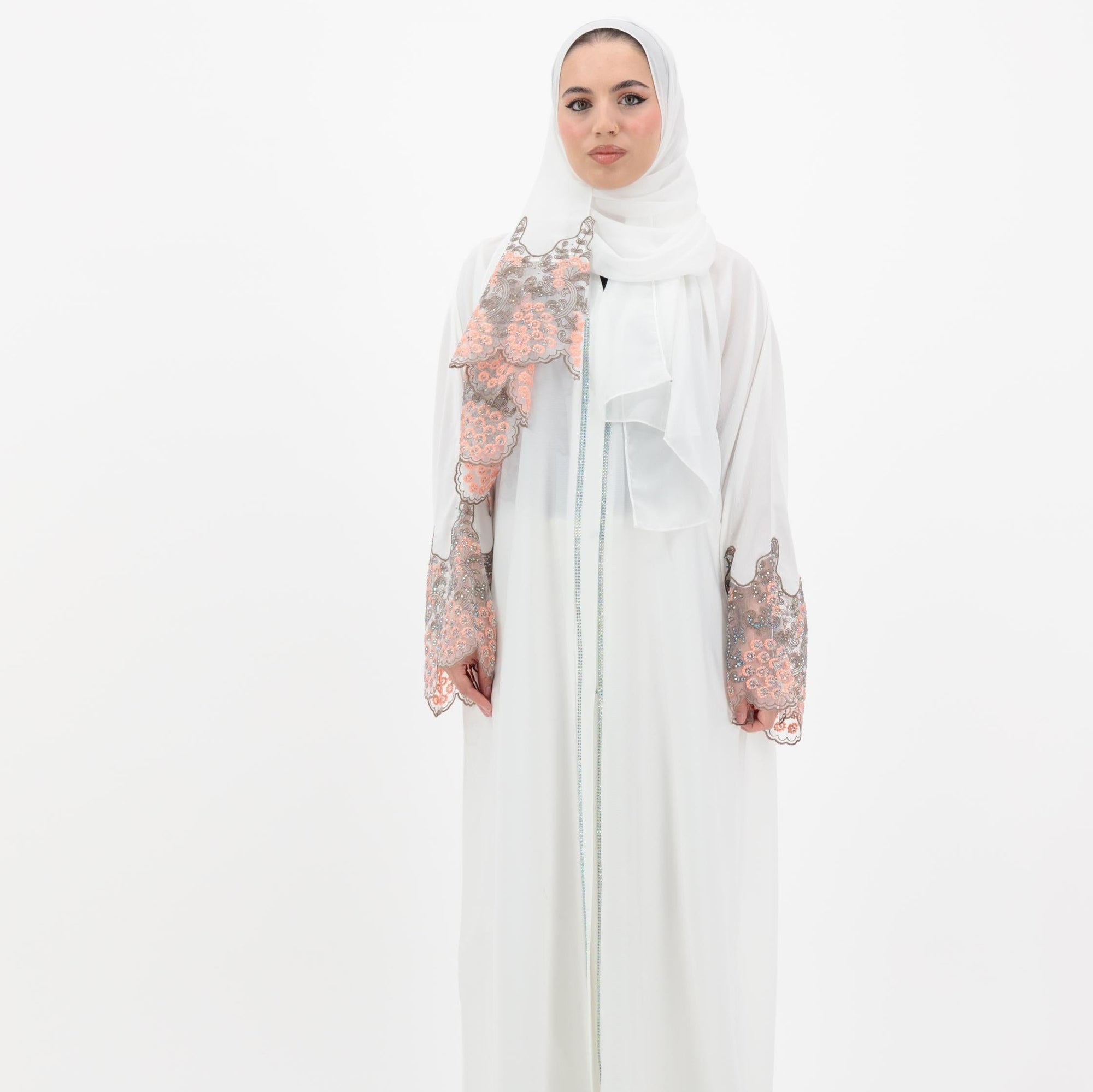 White abaya with silver beadwork and pink and brown embroidery on the sleeves. Made from crepe material with popper buttons, available in sizes 50-60, and includes a matching hijab.