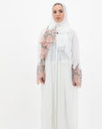 White abaya with silver beadwork and pink and brown embroidery on the sleeves. Made from crepe material with popper buttons, available in sizes 50-60, and includes a matching hijab.