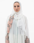 White abaya with silver beadwork and pink and brown embroidery on the sleeves. Made from crepe material with popper buttons, available in sizes 50-60, and includes a matching hijab.