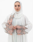 White abaya with silver beadwork and pink and brown embroidery on the sleeves. Made from crepe material with popper buttons, available in sizes 50-60, and includes a matching hijab.