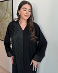 A luxurious black Nidha-lined open abaya featuring intricate black beaded and furry detailing, designed for elegance and comfort. Includes convenient popper buttons and a complimentary hijab for a polished look. Perfect for any occasion with a soft, breathable, and flowy fit.