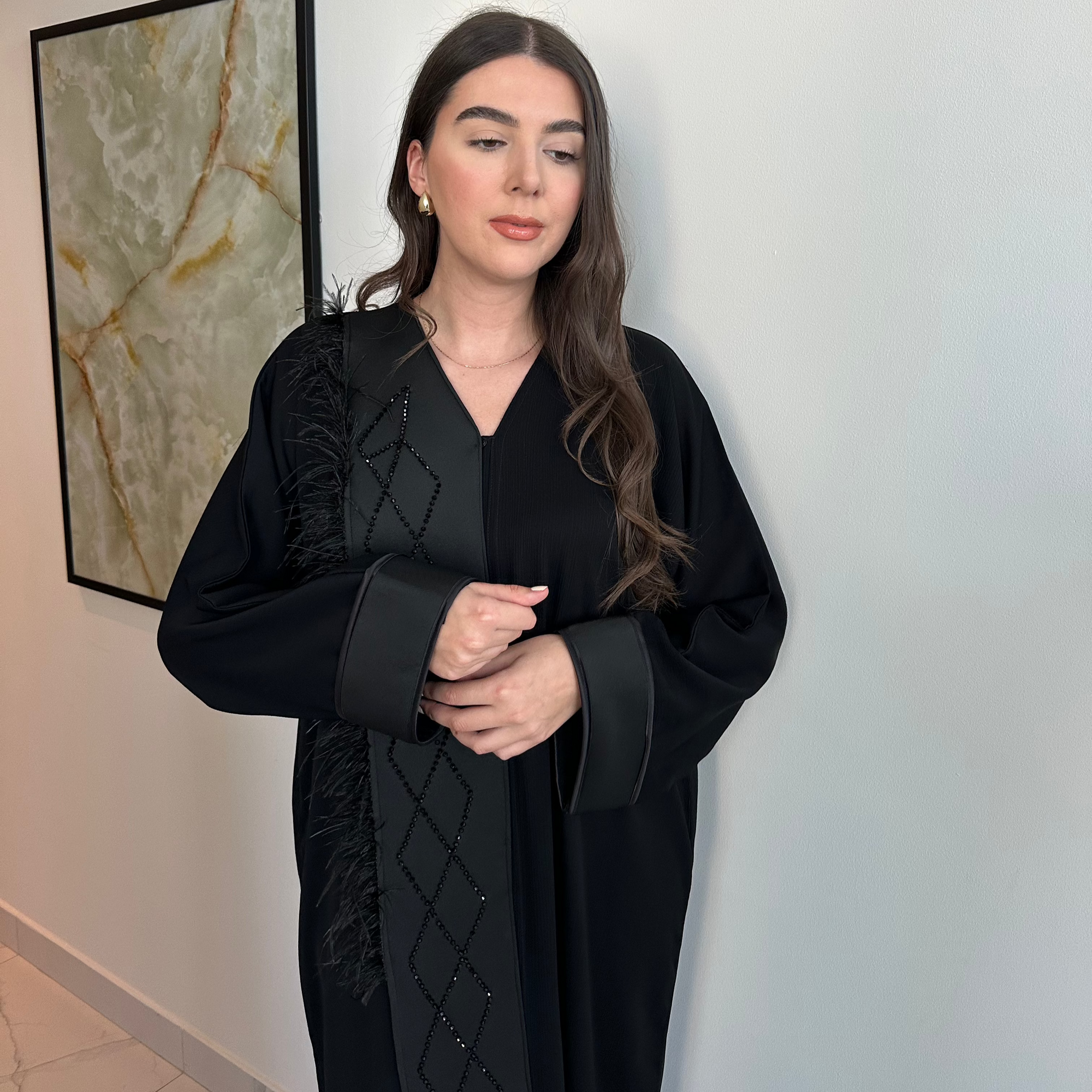 A luxurious black Nidha-lined open abaya featuring intricate black beaded and furry detailing, designed for elegance and comfort. Includes convenient popper buttons and a complimentary hijab for a polished look. Perfect for any occasion with a soft, breathable, and flowy fit.