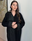 A luxurious black Nidha-lined open abaya featuring intricate black beaded and furry detailing, designed for elegance and comfort. Includes convenient popper buttons and a complimentary hijab for a polished look. Perfect for any occasion with a soft, breathable, and flowy fit.