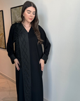 A luxurious black Nidha-lined open abaya featuring intricate black beaded and furry detailing, designed for elegance and comfort. Includes convenient popper buttons and a complimentary hijab for a polished look. Perfect for any occasion with a soft, breathable, and flowy fit.