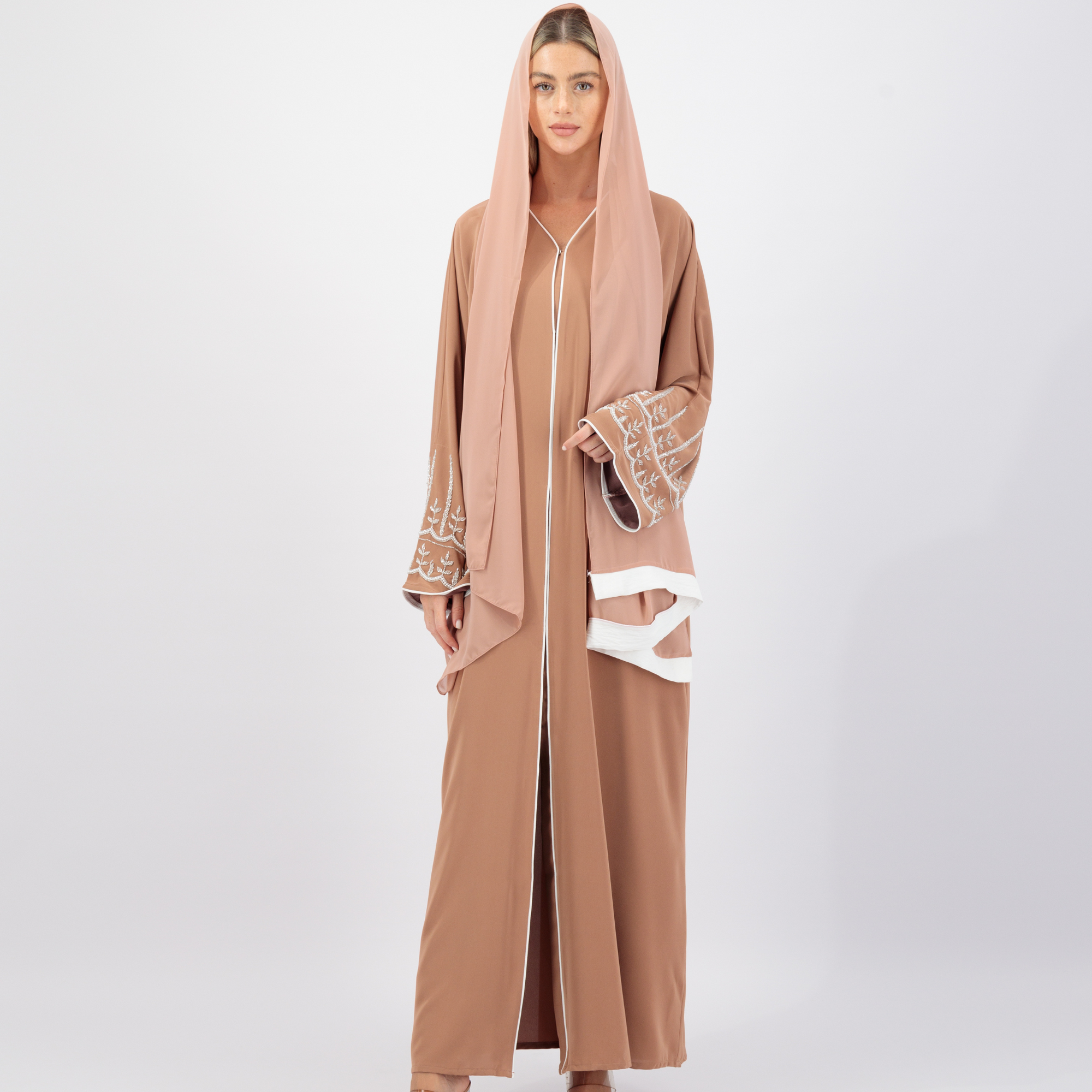 The Sapna Abaya features silver beaded sleeves, popper buttons, and a white line detail. Available in black, beige, brown, and white, made from Zoom fabric in sizes 50-60. Includes a matching hijab.