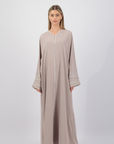 The Sapna Abaya features silver beaded sleeves, popper buttons, and a white line detail. Available in black, beige, brown, and white, made from Zoom fabric in sizes 50-60. Includes a matching hijab.